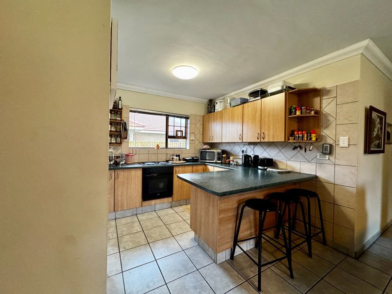A functional kitchen featuring laminate cabinetry, tiled backsplash, built-in oven, electric hob, and a breakfast bar with tiled flooring.