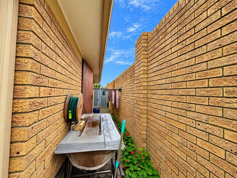A narrow side passage featuring face brick walls, a paved walkway, and a wall-mounted clothesline leading to a small storage shed.