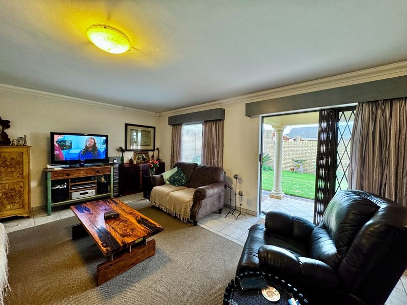 A comfortable living room featuring tiled flooring, a ceiling light fixture, and a sliding glass door providing direct access to the rear patio and garden.