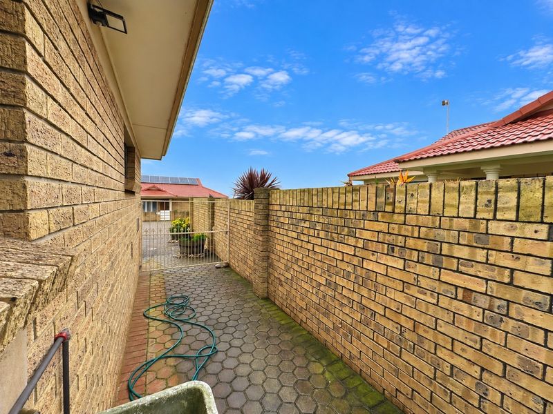 A side walkway featuring brick boundary walls and paved flooring, leading to a metal security gate at the rear of the property.
