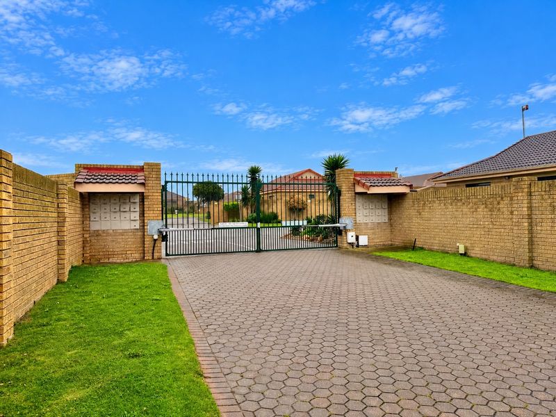 Secure gated entrance to the property complex featuring brick boundary walls, a paved driveway, and integrated communal post boxes.