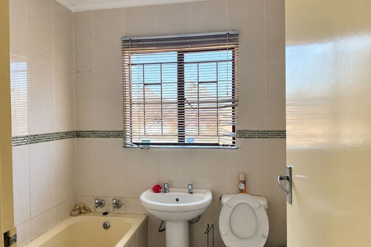 A functional bathroom featuring a pedestal basin, bathtub, and toilet with neutral wall tiling and security bars on the window.