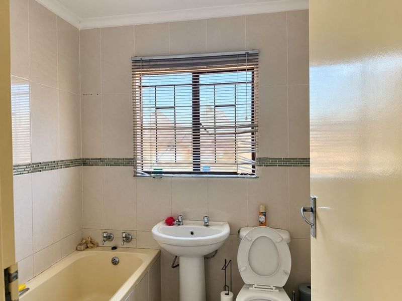 A functional bathroom featuring a pedestal basin, bathtub, and toilet with neutral wall tiling and security bars on the window.