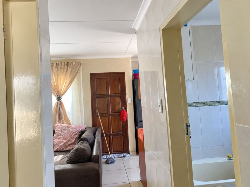 A view from a tiled hallway looking into a living area and a bathroom featuring tiled walls and a bathtub.