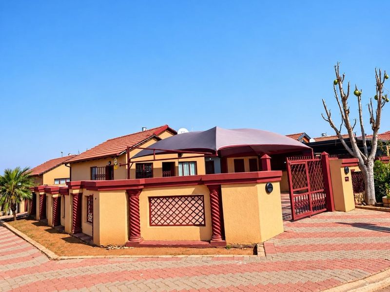 Front exterior view of a house featuring a paved driveway, decorative perimeter wall with columns, and a shaded parking area.