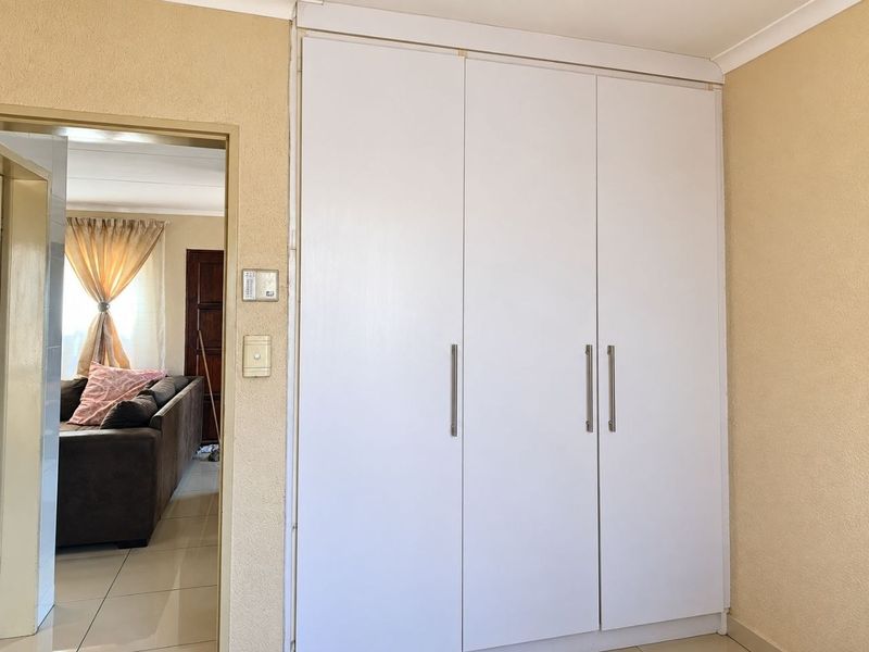 A bedroom featuring white built-in cupboards with modern handles, with a view into the adjacent living area.