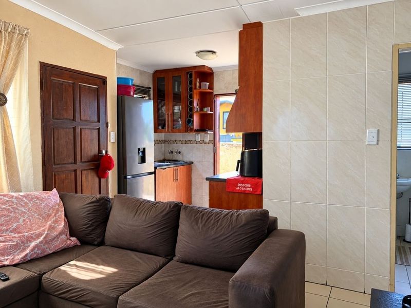 Open plan living area featuring a functional kitchen with wooden cabinetry, tiled splashbacks, and direct access to the exterior.