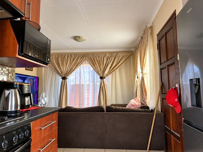 Open plan kitchen and living area featuring wooden cabinetry, dark countertops, built-in oven, and tiled flooring with direct access to the living space.