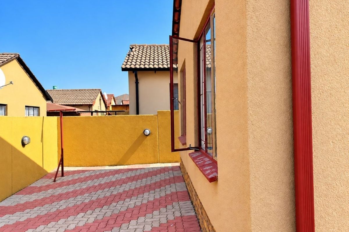 A side view of the property showing a paved patio area, boundary wall, and exterior wall finishes with a red downpipe.