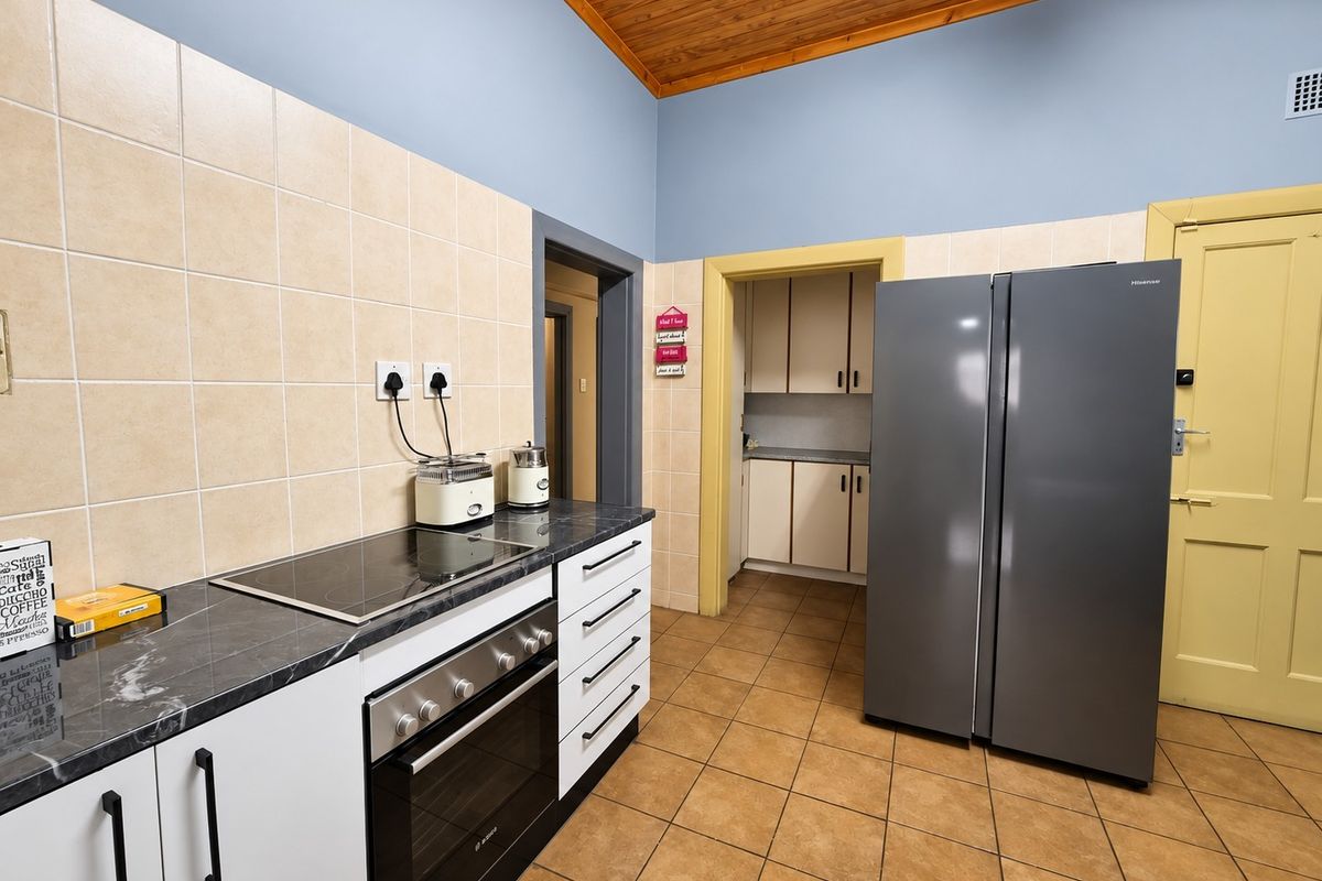 A functional kitchen featuring a built-in oven, electric hob, tiled splashback, and tiled flooring, with an adjacent scullery area visible.