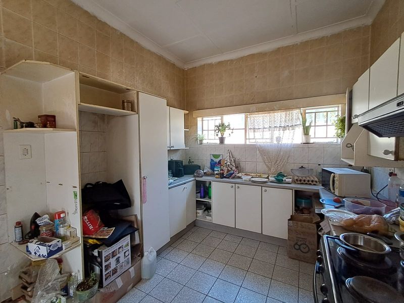 A dated kitchen featuring original cabinetry, tiled splashbacks, and tiled flooring, offering significant potential for a modern renovation and layout update.