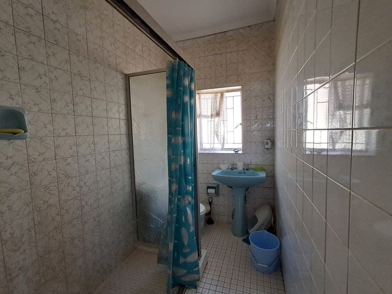 A functional bathroom featuring a pedestal basin, shower enclosure, and fully tiled walls and floors, requiring cosmetic updates to modernize the space.