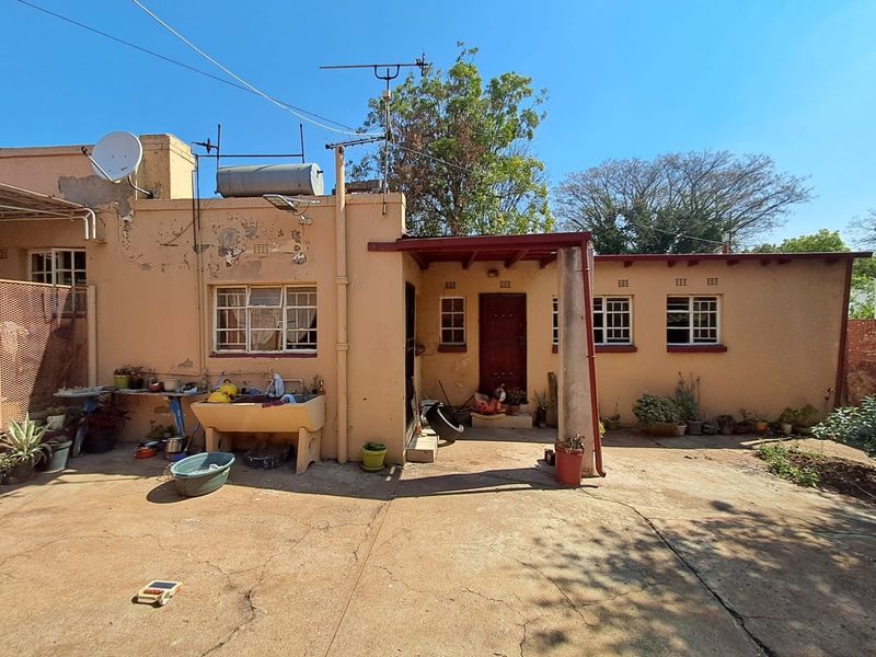 Rear exterior view of the property featuring a concrete patio area, external wash basin, and weathered wall finishes requiring maintenance.