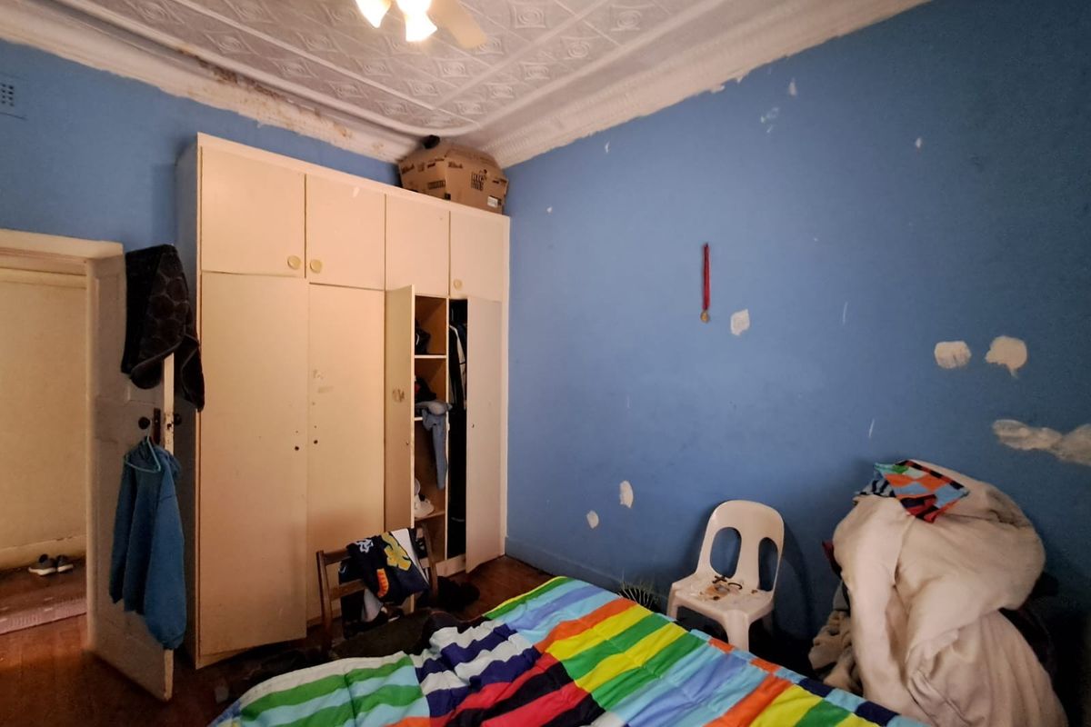 Bedroom featuring a pressed metal ceiling, built-in wardrobe, and timber flooring, currently requiring cosmetic repairs and repainting.