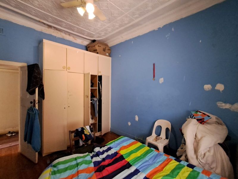 Bedroom featuring a pressed metal ceiling, built-in wardrobe, and timber flooring, currently requiring cosmetic repairs and repainting.