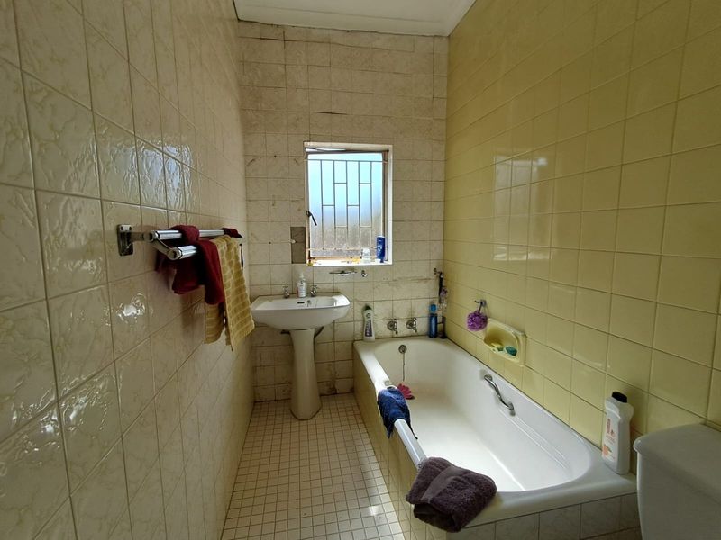 A dated bathroom featuring a pedestal basin, built-in bathtub, and full-height ceramic wall tiling, offering potential for a modern renovation.