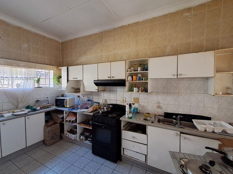 A dated kitchen featuring original cabinetry, tiled splashbacks, and floor tiles, offering significant potential for a modern renovation and layout update.