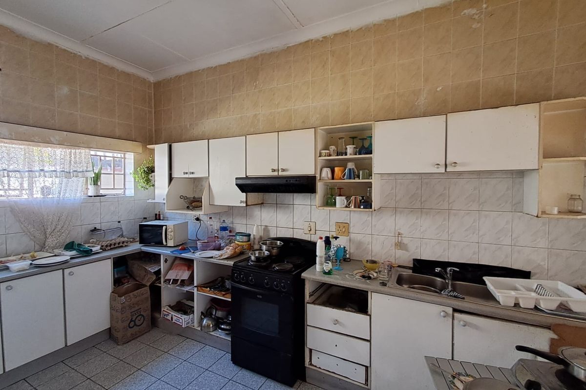 A dated kitchen featuring original cabinetry, tiled splashbacks, and floor tiles, offering significant potential for a modern renovation and layout update.
