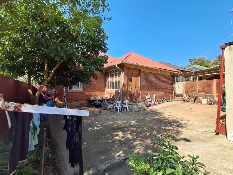 Rear view of a brick house featuring a metal roof, concrete paved yard, and perimeter boundary walls.