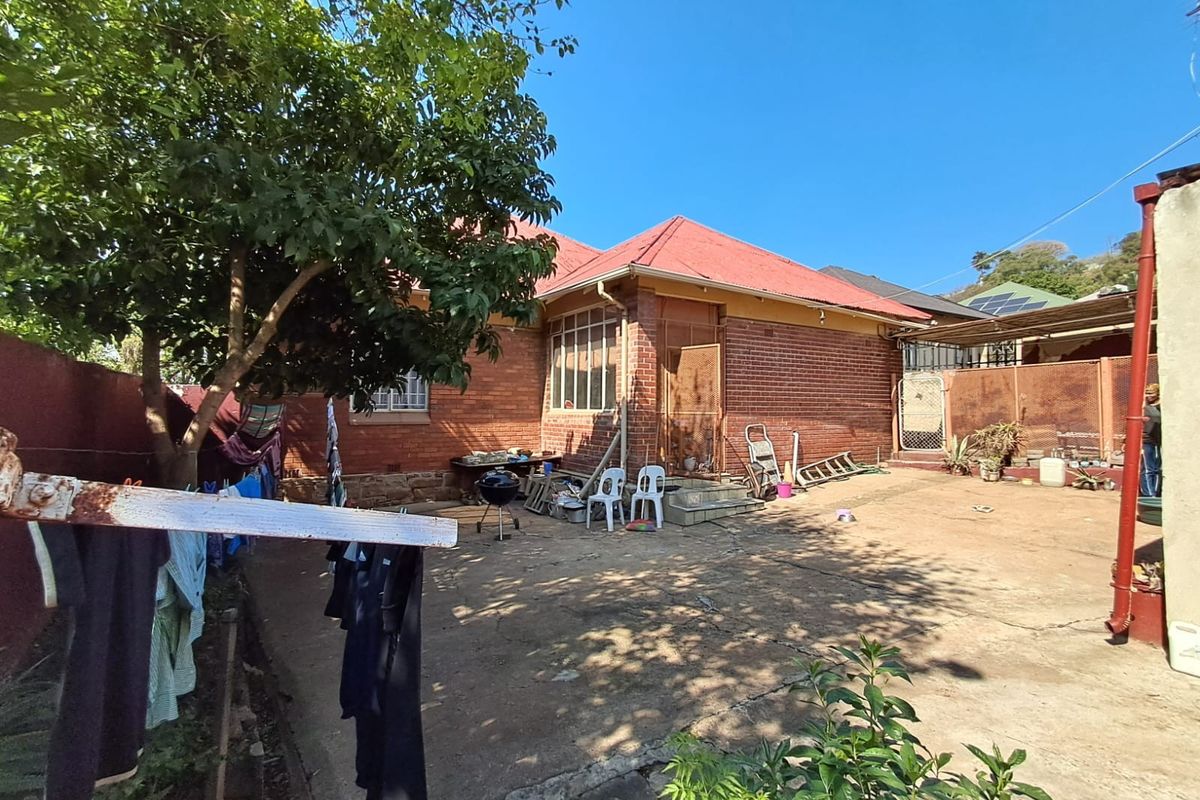 Rear view of a brick house featuring a metal roof, concrete paved yard, and perimeter boundary walls.
