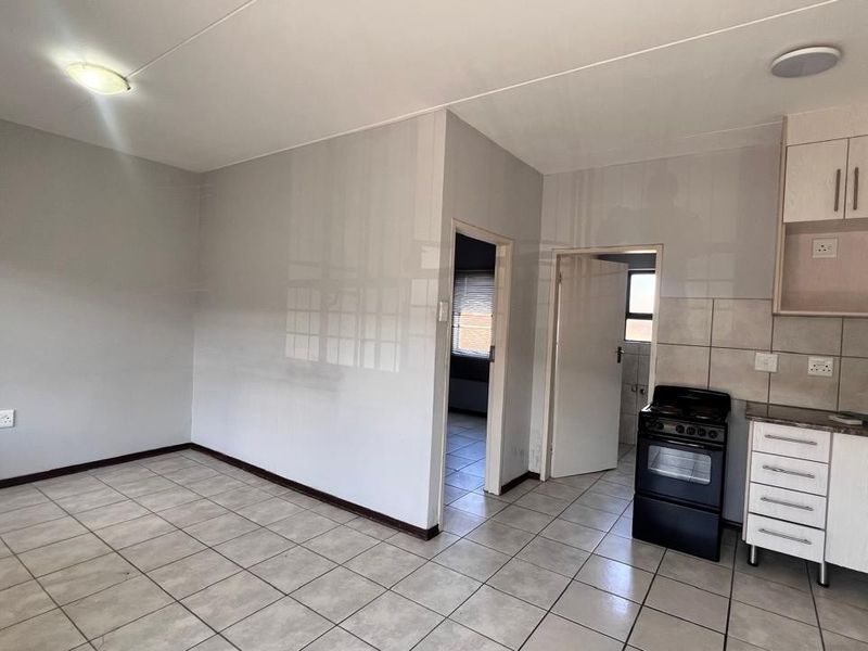An open-plan living and kitchen area featuring neutral tiled flooring, built-in cabinetry, and a freestanding stove, offering a clean and functional layout.