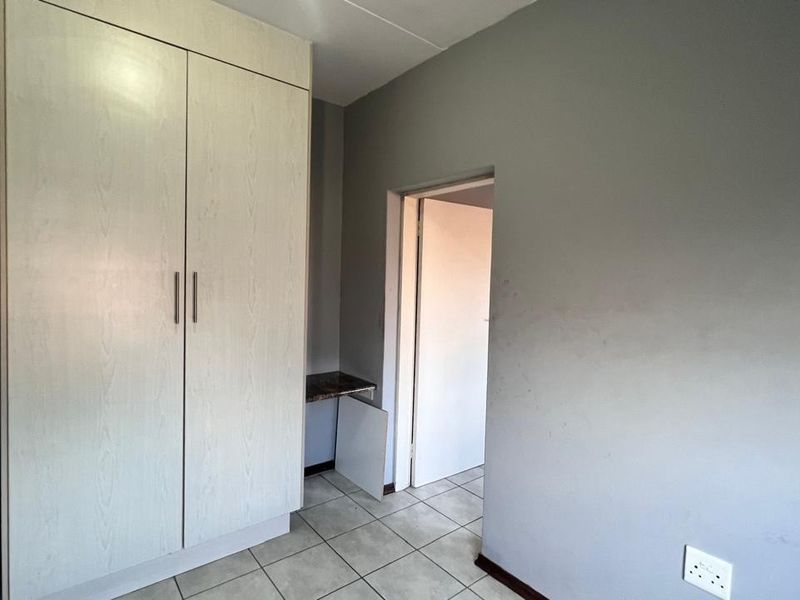 A bedroom featuring tiled flooring and a built-in wardrobe, showing signs of wear on the walls and cabinetry.