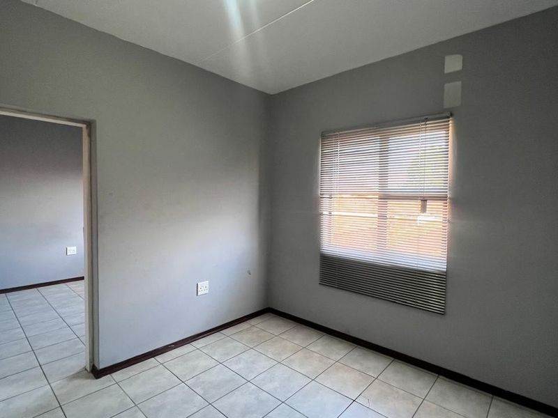 An empty bedroom featuring neutral grey walls, tiled flooring, and fitted venetian blinds, offering a blank canvas for personalization.