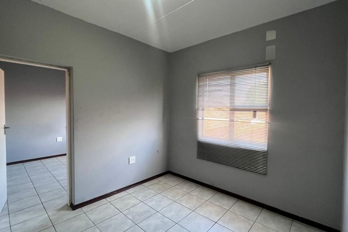 An empty bedroom featuring neutral grey walls, tiled flooring, and fitted venetian blinds, offering a blank canvas for personalization.