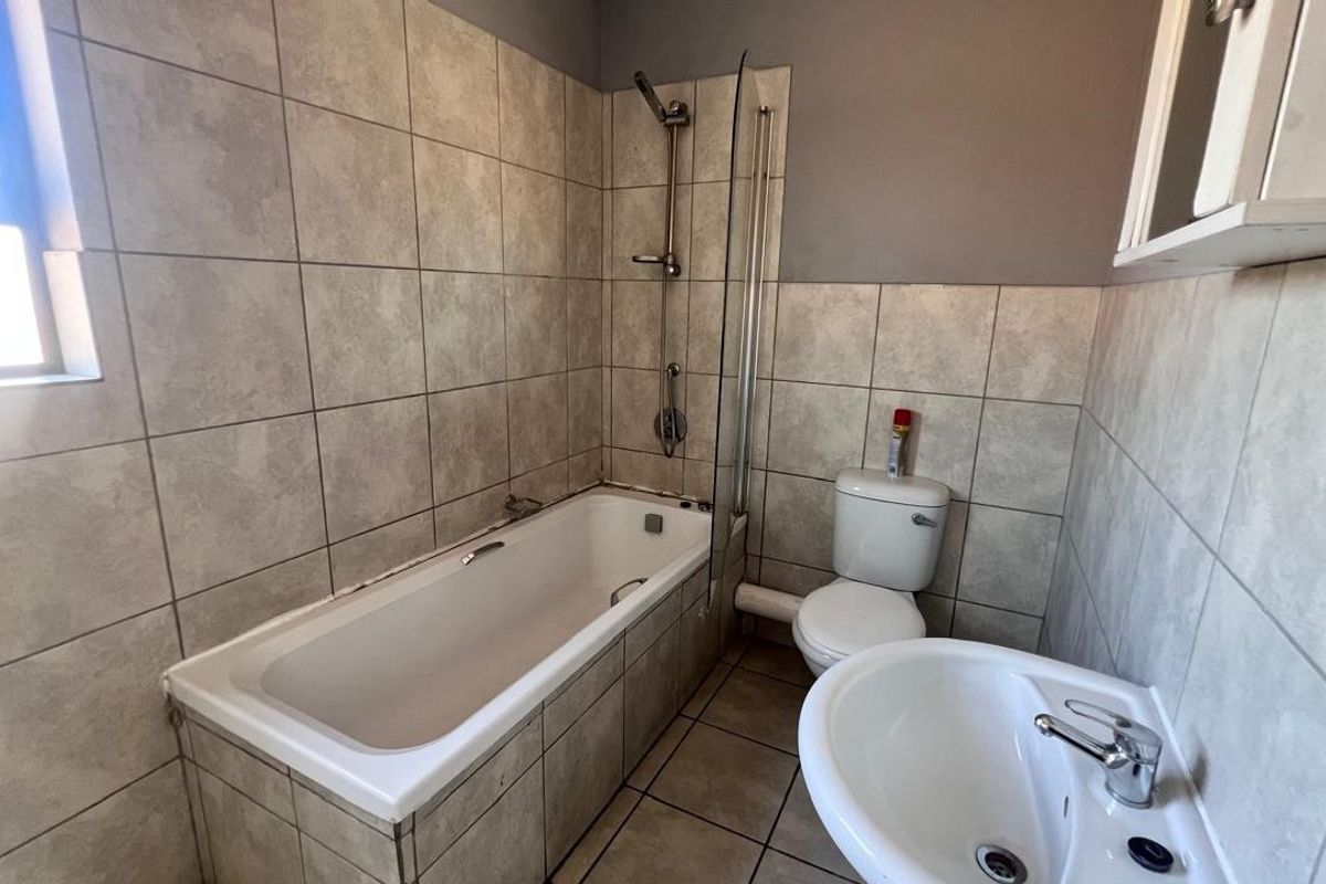 A functional bathroom featuring a bathtub with a shower attachment, glass screen, pedestal sink, and toilet, finished with neutral wall and floor tiling.