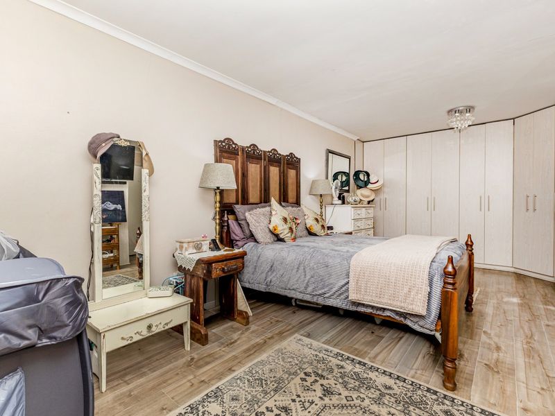 A well-maintained bedroom featuring wood-look tile flooring, neutral wall finishes, and extensive built-in cupboard storage.