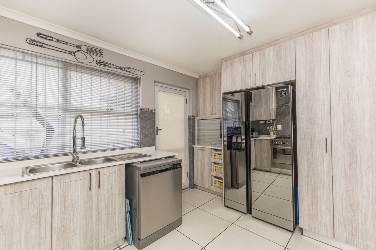 A functional kitchen featuring light wood-grain cabinetry, tiled flooring, a double sink with a gooseneck faucet, and integrated appliances.