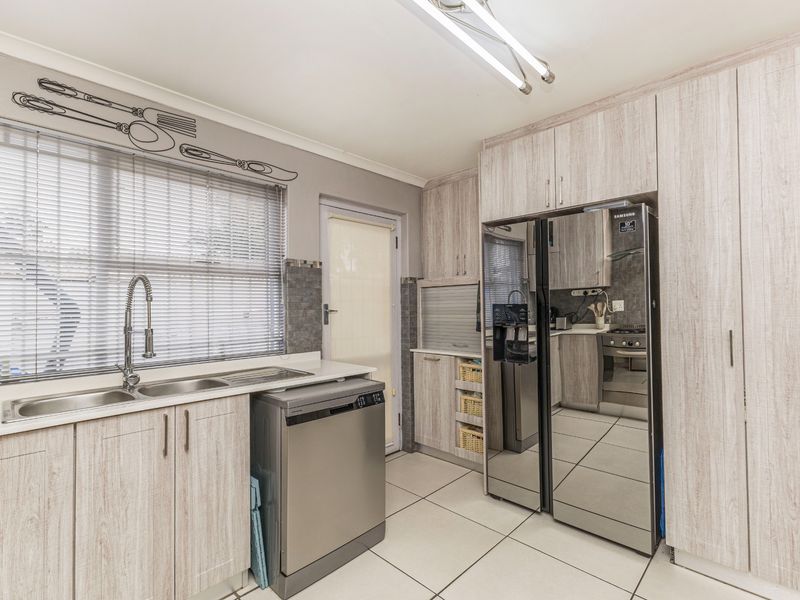 A functional kitchen featuring light wood-grain cabinetry, tiled flooring, a double sink with a gooseneck faucet, and integrated appliances.