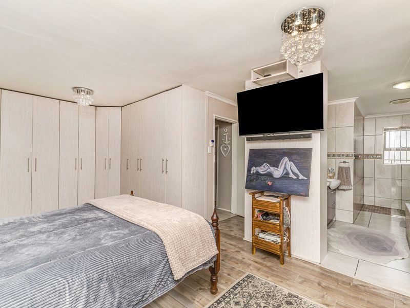 Spacious bedroom featuring extensive built-in cabinetry, laminate flooring, and an open-plan en-suite bathroom with tiled finishes and modern lighting.