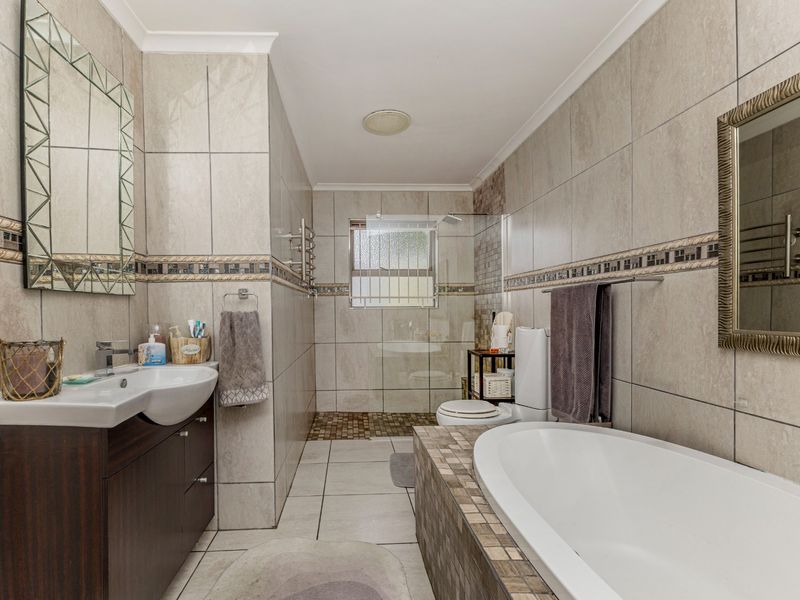 A well-appointed bathroom featuring a built-in bathtub, a separate tiled shower enclosure, a vanity cabinet with a basin, and a heated towel rail.