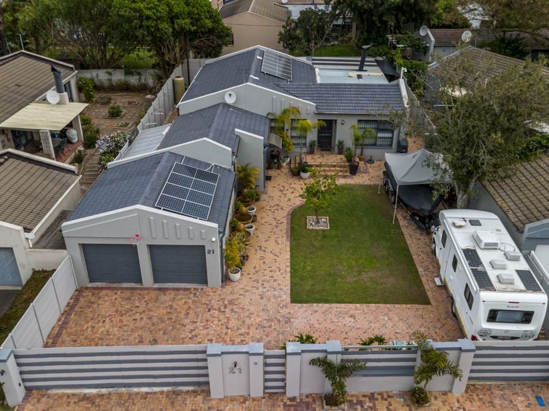 Aerial view of a residential property featuring a double garage, solar panels, paved driveway, and a well-maintained front garden with boundary walling.