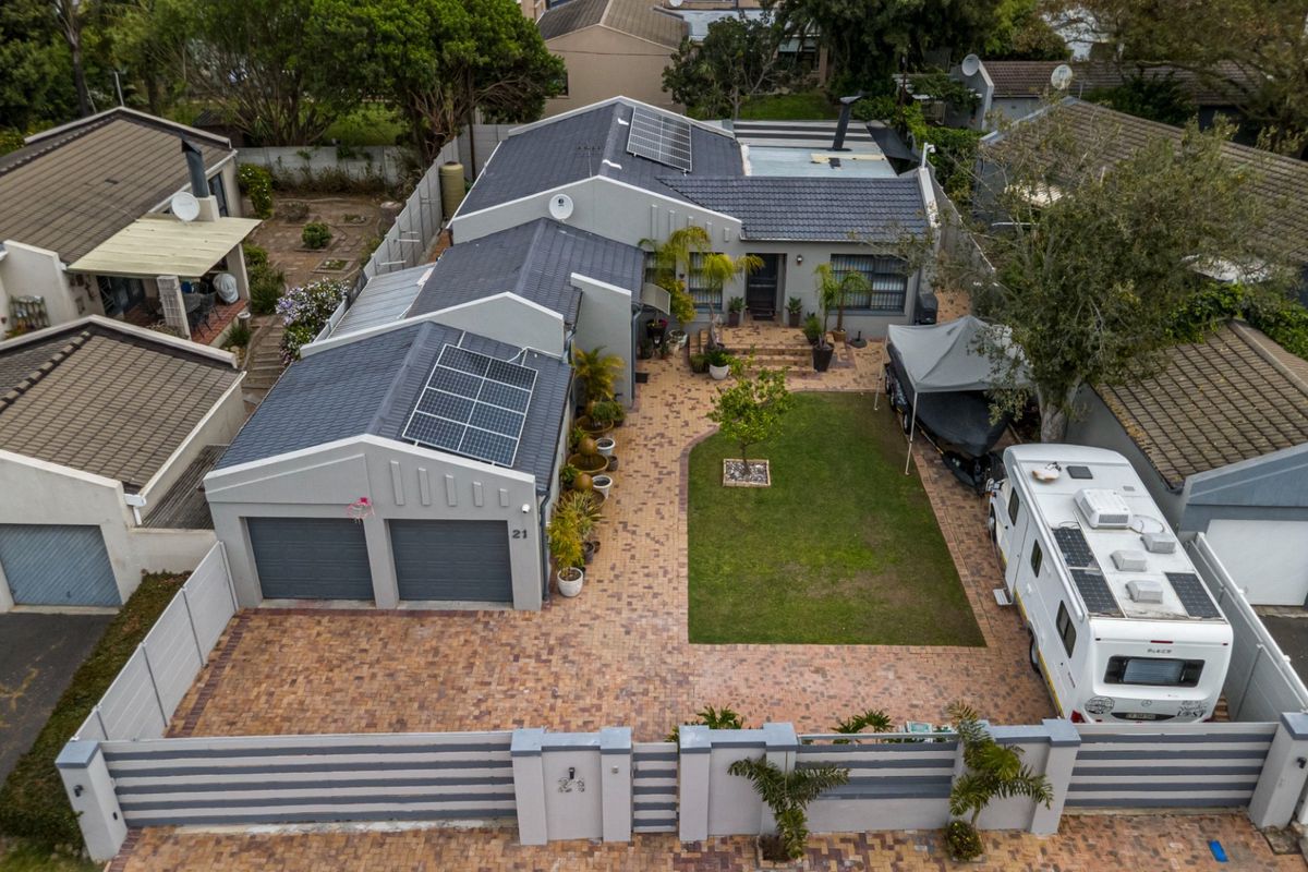 Aerial view of a residential property featuring a double garage, solar panels, paved driveway, and a well-maintained front garden with boundary walling.