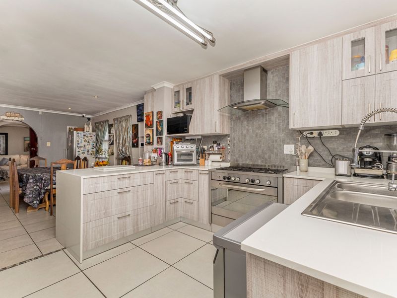 An open-plan kitchen featuring light wood-grain cabinetry, stone countertops, a gas stove with extractor fan, and tiled flooring, flowing into the adjacent dining area.