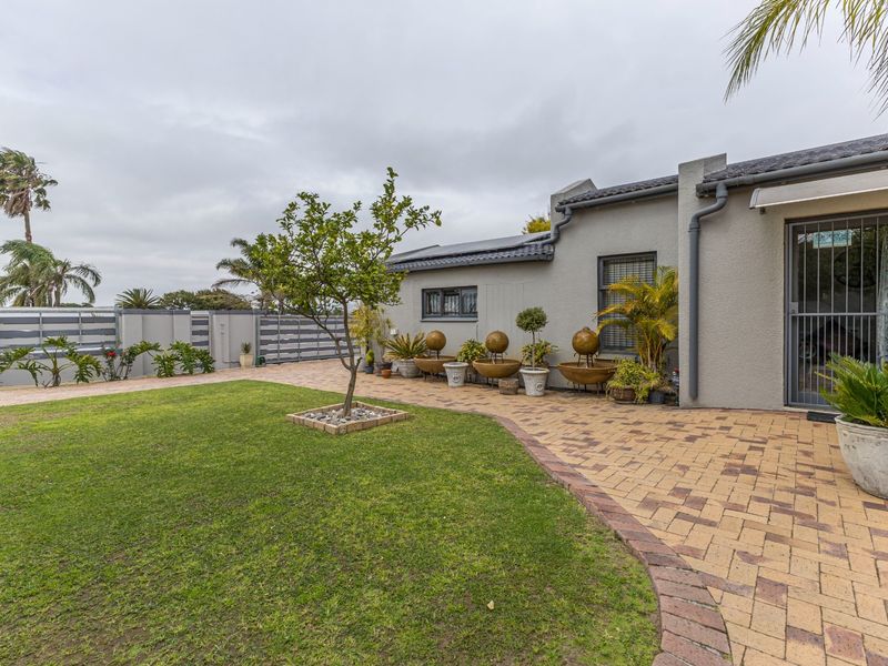 A well-maintained rear garden featuring a paved patio area, manicured lawn, and secure boundary walling with integrated security features.