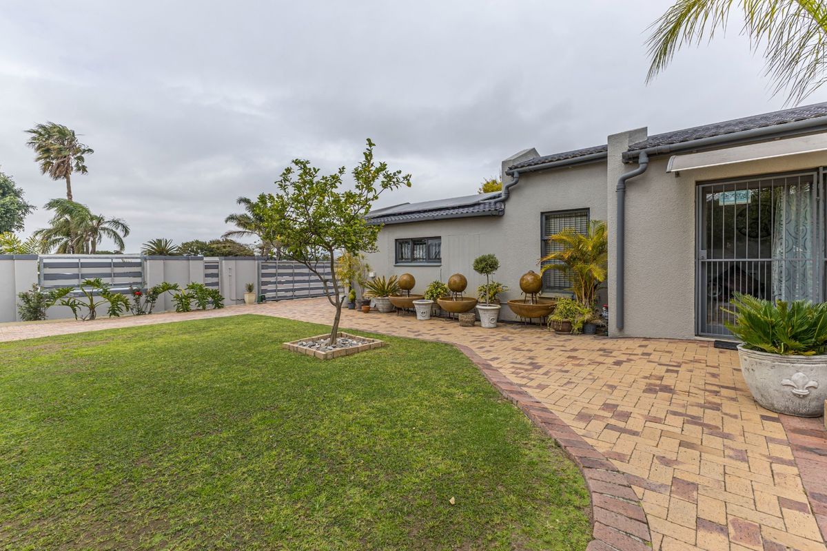 A well-maintained rear garden featuring a paved patio area, manicured lawn, and secure boundary walling with integrated security features.