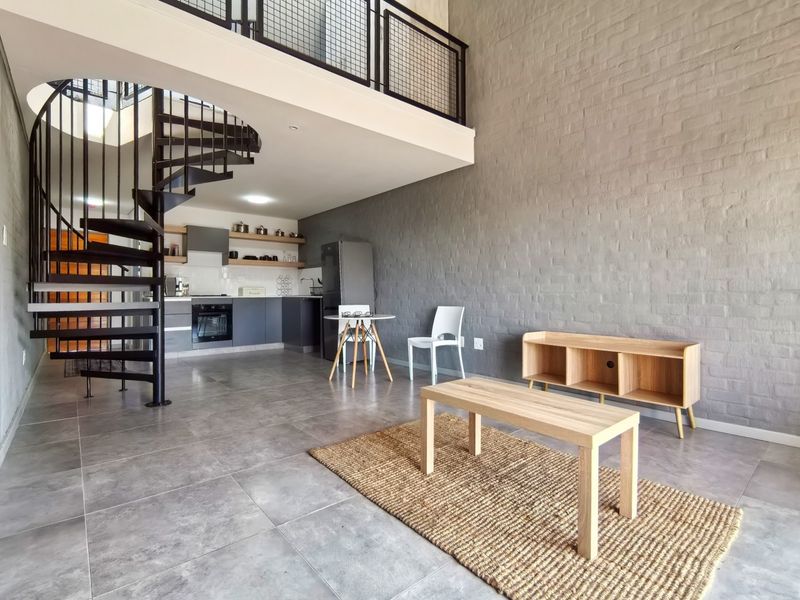 Modern open-plan living area featuring a striking spiral staircase, mezzanine level, exposed brick wall, and a contemporary kitchen with built-in appliances.