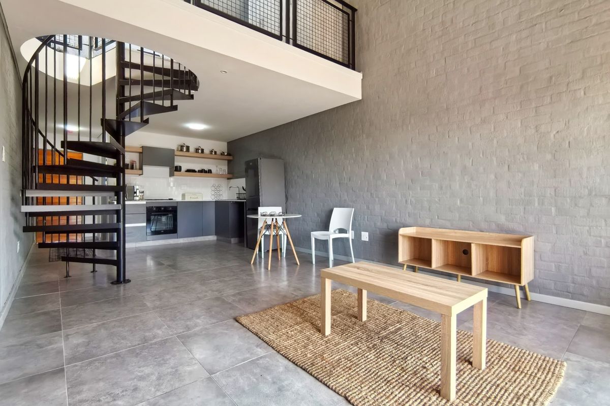 Modern open-plan living area featuring a striking spiral staircase, mezzanine level, exposed brick wall, and a contemporary kitchen with built-in appliances.