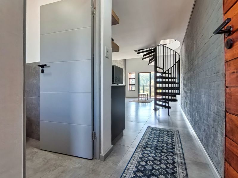 Modern open-plan living area featuring a striking black spiral staircase, tiled flooring, and an exposed brick feature wall leading to a balcony.