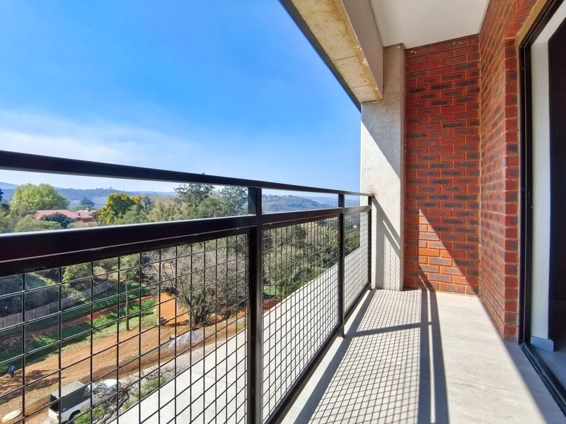 A modern balcony featuring a metal balustrade, exposed brick wall, and scenic views over the surrounding landscape.