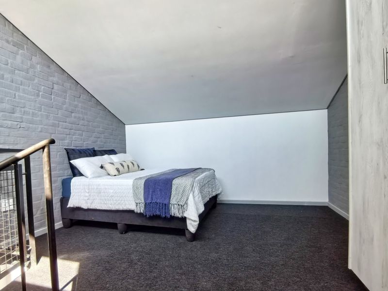 A loft-style bedroom featuring an exposed brick wall, sloped ceiling, and built-in wardrobe storage.