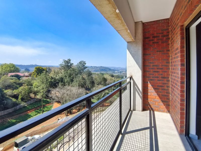 A clean, modern balcony featuring exposed brickwork, a secure metal balustrade, and expansive views over the surrounding landscape.