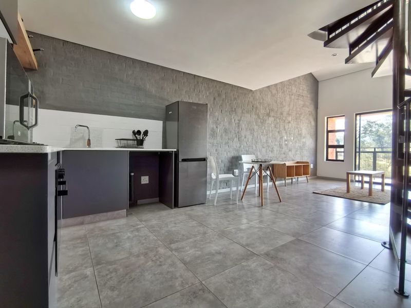 Modern open-plan living area featuring a sleek kitchen with stone countertops, tiled flooring, a textured feature wall, and a spiral staircase.