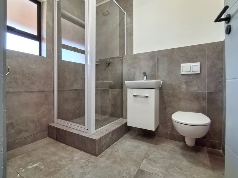 Modern bathroom featuring a glass shower enclosure, wall-mounted vanity, and wall-hung toilet with neutral grey tiling throughout.