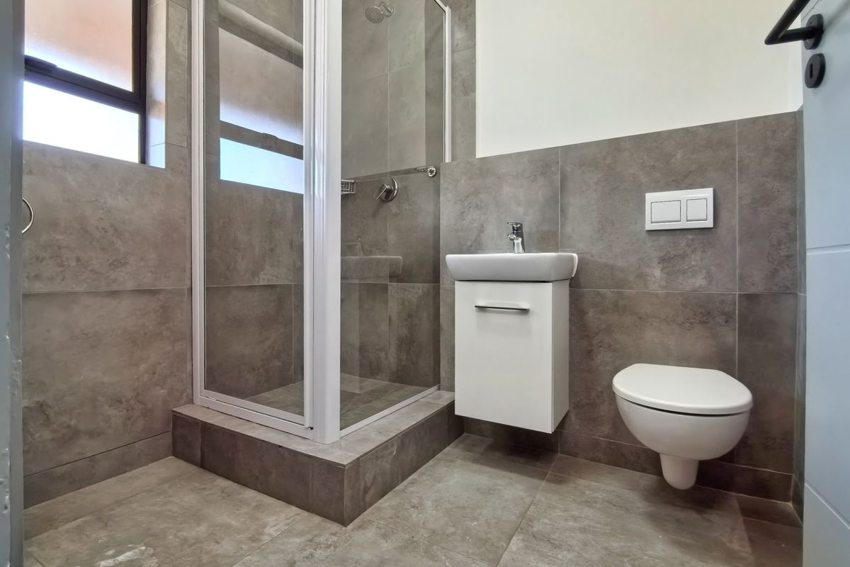 Modern bathroom featuring a glass shower enclosure, wall-mounted vanity, and wall-hung toilet with neutral grey tiling throughout.