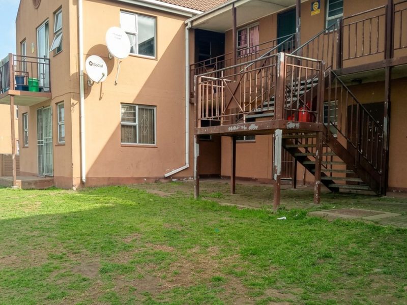 Rear exterior view of an apartment building featuring a communal lawn area and an external metal staircase providing access to upper levels.