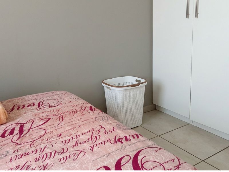 A bedroom featuring neutral wall tones, white built-in cupboards, and tiled flooring.